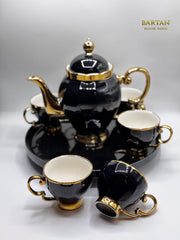 Black and gold ceramic tea set with teapot, cups, and saucers on a white background.