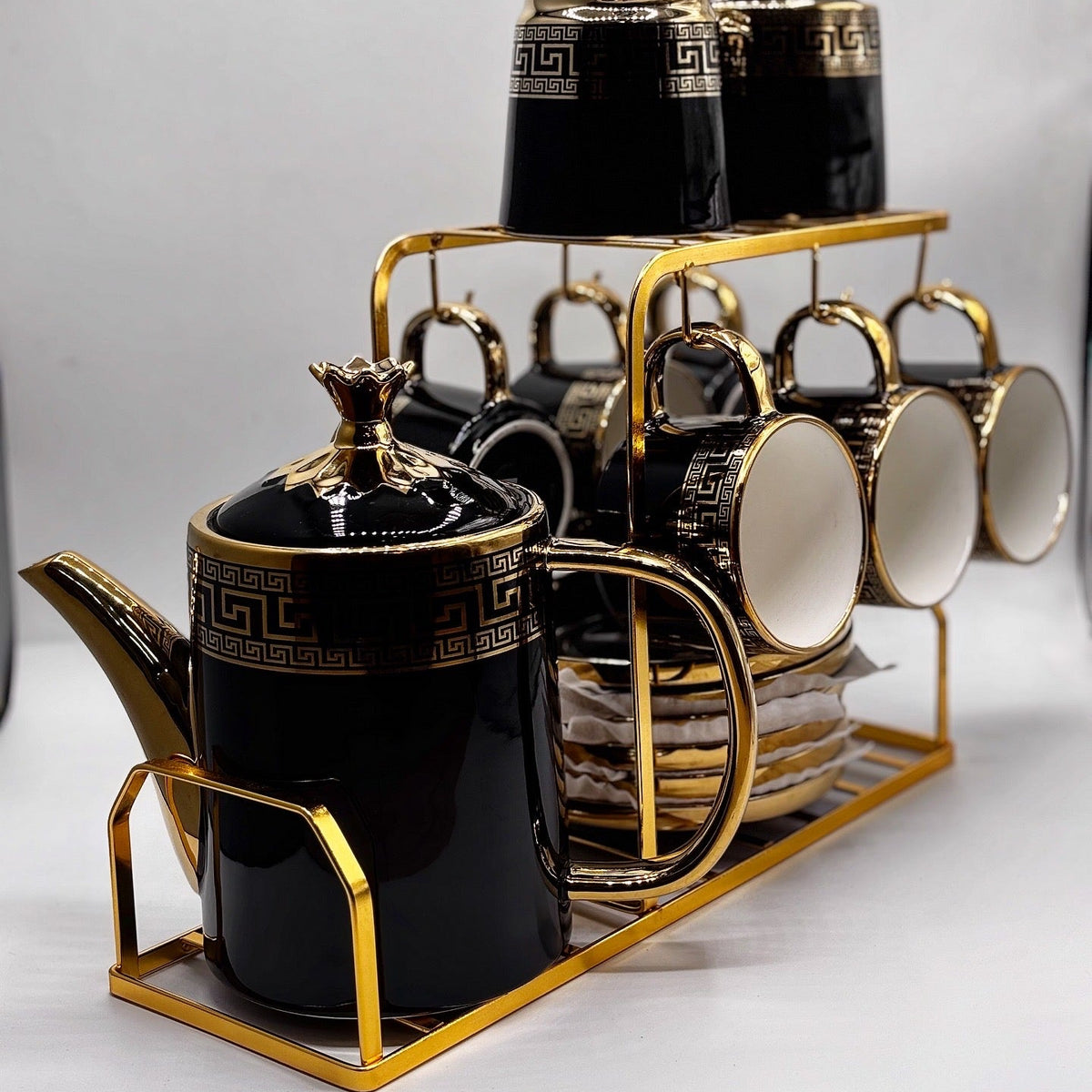 Black and gold ceramic tea set with teapot, cups, and saucers on a white background.