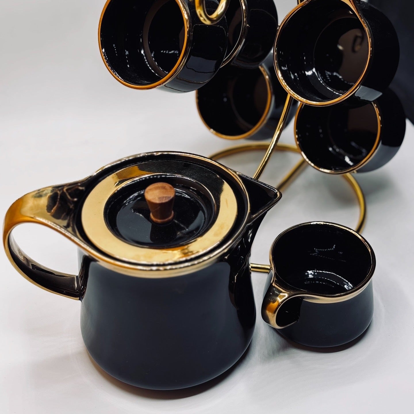 Black teapot with gold accents and matching cups on a white background